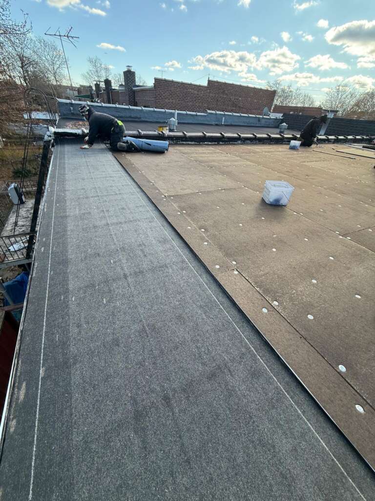Flat roof installation in progress at Country Club, Bronx. Roofing team removing old roof, preparing deck, installing insulation and waterproof membrane for long-lasting protection